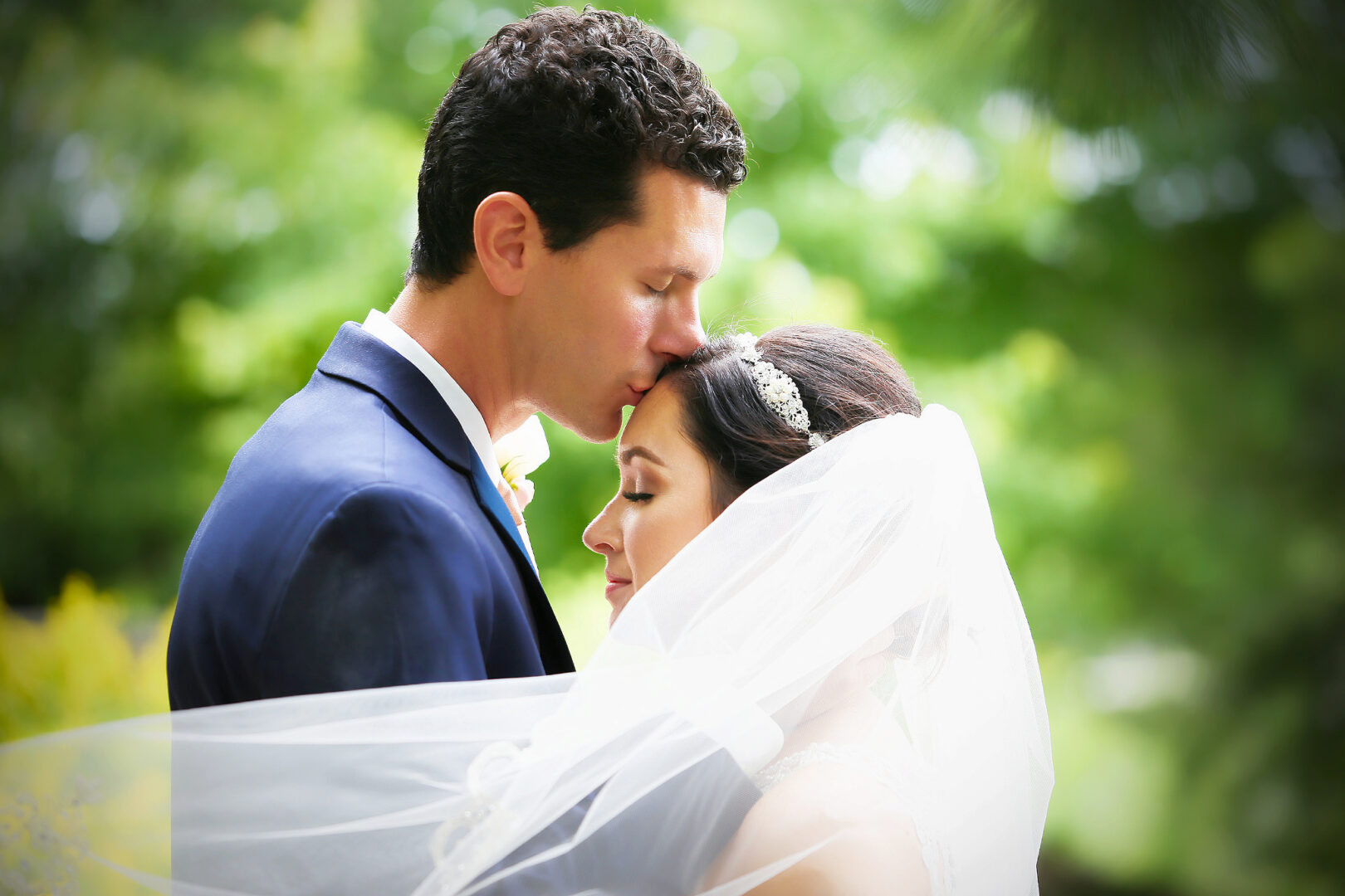 A kiss on the forehead by the groom with her veil flowing in the wind