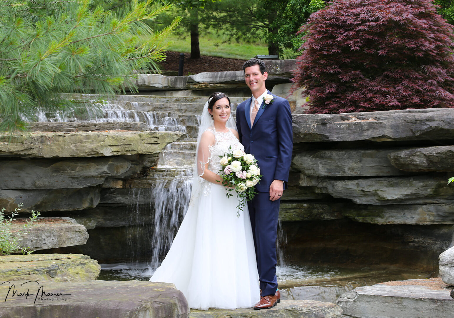 bride and groom posing near a waterfall